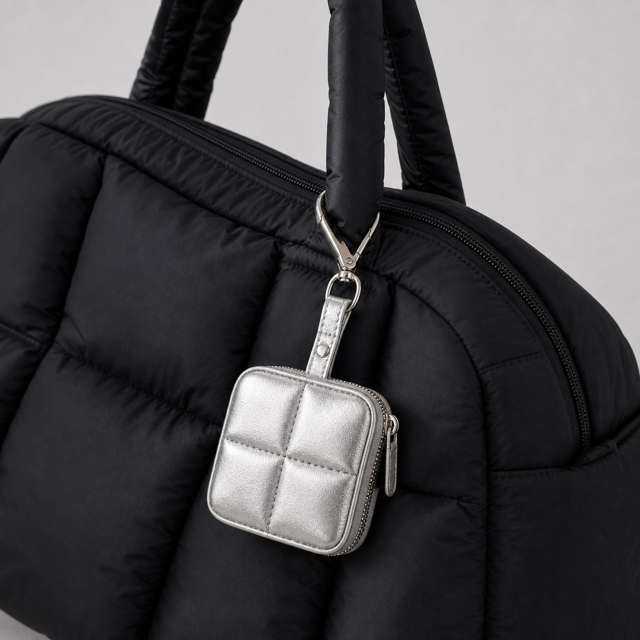 Metallic silver quilted tiny tech pouch clipped to a black padded bag